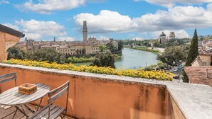 Ein Balkon mit Tisch und Stühlen mit Blick auf einen Fluss, im Hintergrund Gebäude und ein Turm.