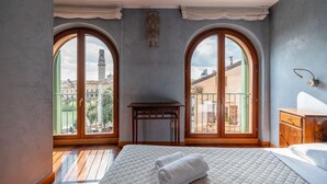 A bedroom with a large bed, a small table, and two arched windows with a city view. - Ponte Pietra Residence (Verona)