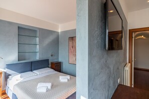 A modern hotel room with a large bed, a built-in shelf, a mirror, and a radiator. - Ponte Pietra Residence (Verona)