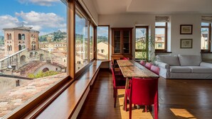 Ein geräumiges Zimmer mit großem Fenster und Blick auf eine historische Stadtansicht, einem Holzespeisetisch und einem modernen Sofa.
