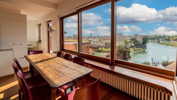 Ein Essbereich mit einem großen Holztisch und roten Stühlen, mit Blick auf einen Fluss und historische Gebäude.