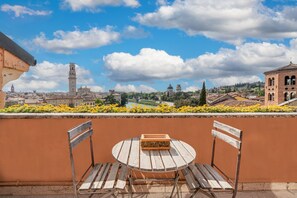 A balcony with a round wooden table and two chairs, overlooking a cityscape with historic buildings and a river.
