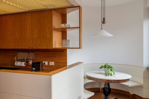 A modern kitchen with wooden cabinets, a white countertop, a round table with a plant, and a hanging light fixture. - Ponte Pietra Residence (Verona)