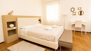 A neatly arranged bedroom with a bed, bedside table, lamp, and a desk with chairs.