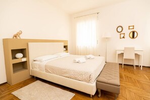 A neatly arranged bedroom with a bed, bedside table, lamp, and a desk with chairs.
