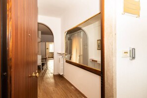 A hallway with wooden flooring, a white door with a brass handle, and a large mirror reflecting a bathroom with a shower and a towel rack. - Serego Residence - Elegant residence overlooking Porta Leoni (Verona)