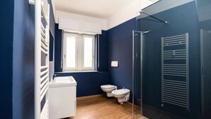 A bathroom with a wooden floor, a white sink, a toilet, and a shower area.