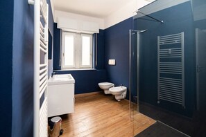 A bathroom with a wooden floor, a white sink, a toilet, and a shower area.