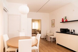A modern kitchen with white cabinets, a black countertop, and a microwave. There is a dining area with a round wooden table and white chairs. - Serego Residence - Elegant residence overlooking Porta Leoni (Verona)