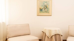 A room with a beige sofa, a small round table with a tablecloth, and a framed painting on the wall. - Serego Residence - Elegant residence overlooking Porta Leoni (Verona)