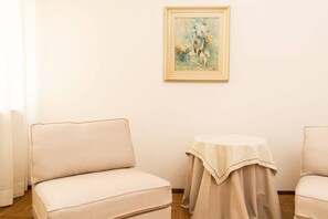 Una habitación con un sofá color beige, una mesita redonda con mantel y un cuadro enmarcado en la pared.