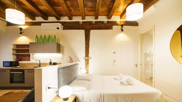 Une chambre d’hôtel moderne dotée d’un grand lit, d’un petit bureau avec une lampe, d’une kitchenette et d’une salle de bain avec un grand miroir.