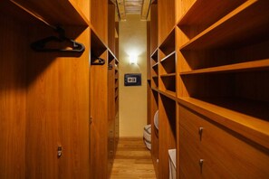 Un petit placard en bois, étroit, avec plusieurs étagères et tiroirs, une tringle pour suspendre les vêtements et un luminaire au plafond.