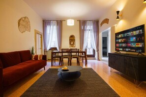 A living room with a red sofa, a black coffee table, a dining area with a table and chairs, and a TV stand with a screen displaying content. - Spacious and elegant Satyr residence with terrace (Verona)