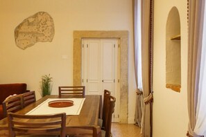 A dining area with a wooden table, chairs, and a decorative plate. There is a white door with a stone wall behind it, and a plant to the left. - Spacious and elegant Satyr residence with terrace (Verona)