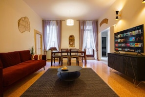 A living room with a red sofa, a black coffee table, a dining area with a table and chairs, and a TV stand with a screen displaying content. - Spacious and elegant Satyr residence with terrace (Verona)