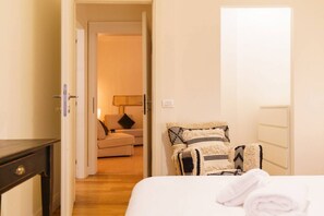 A hotel room with a bed, a bedside table, a chair with patterned cushions, and a sofa in the adjacent room. - Spacious and elegant Satyr residence with terrace (Verona)