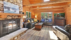 A log cabin interior with a stone fireplace, leather furniture, and a stone wall. - The Lodge at Geneva Lake |Golf Cart |Impressive Log Cabin |Deck |Abbey Springs |Beach |Pools (Fontana-on-Geneva Lake)