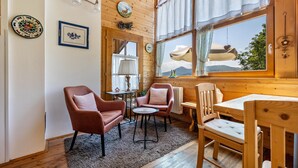 A cozy room with wooden walls, a dining table, two chairs, a small round table, and a window with curtains. - Apartment 'Piccole Dolomiti' with Mountain View, Shared Terrace and Wi-Fi (Brentonico)
