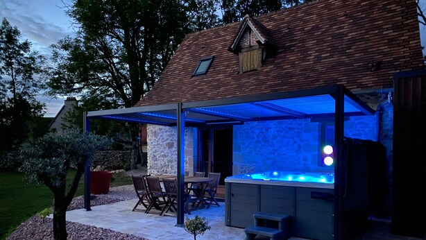 Een overdekt terras buiten met een jacuzzi, stenen muren en een houten dak.