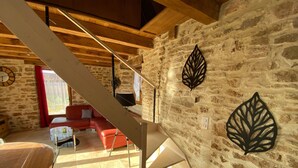 Een rustiek interieur met zichtbare stenen muren, een houten plafond, een trap en een rode bank.