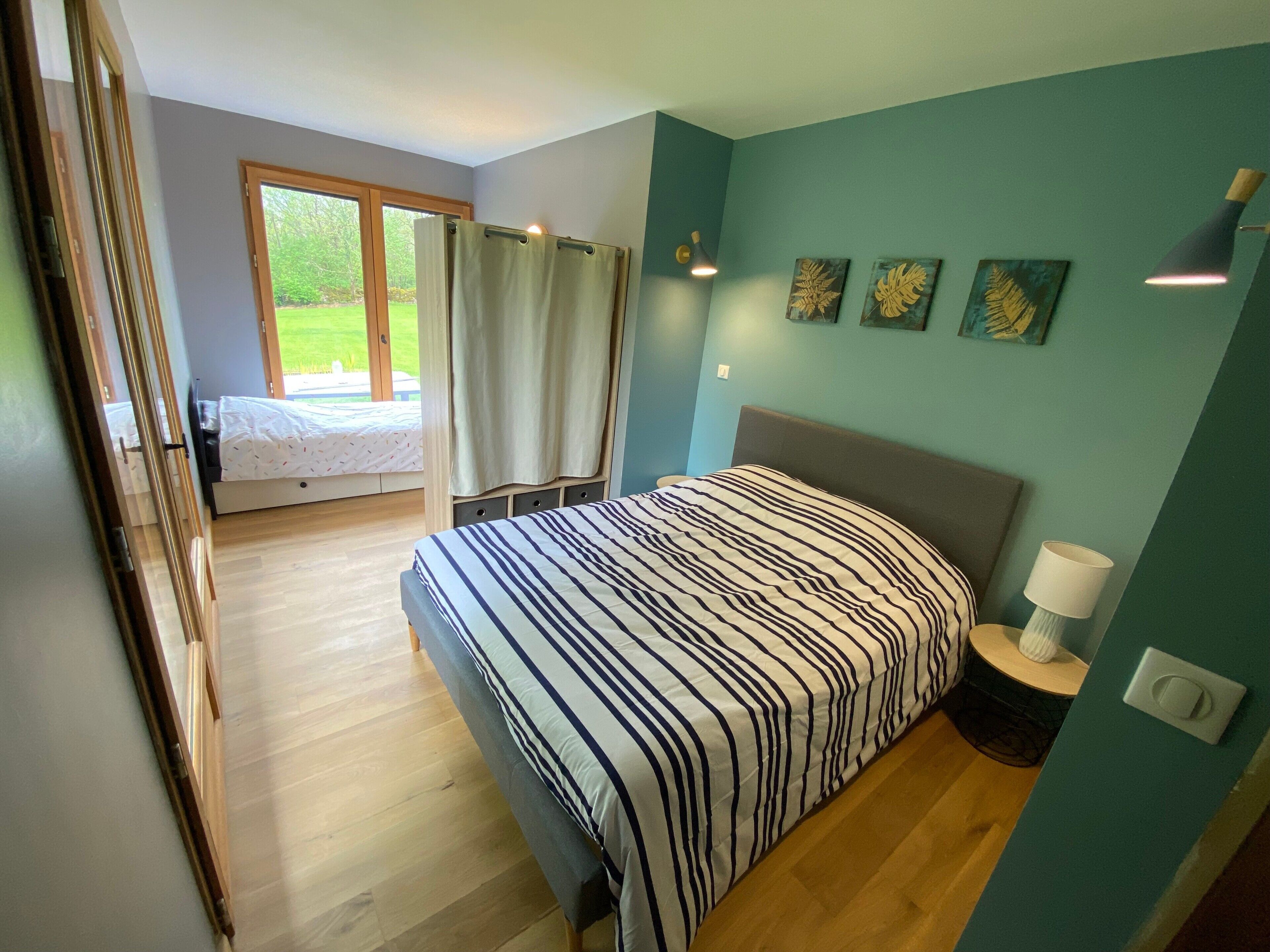 Un dormitorio con cama, ventana con cortinas, lámpara de noche y cuadros en la pared.