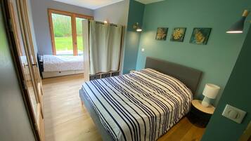 Un dormitorio con cama, ventana con cortinas, lámpara de noche y cuadros en la pared.