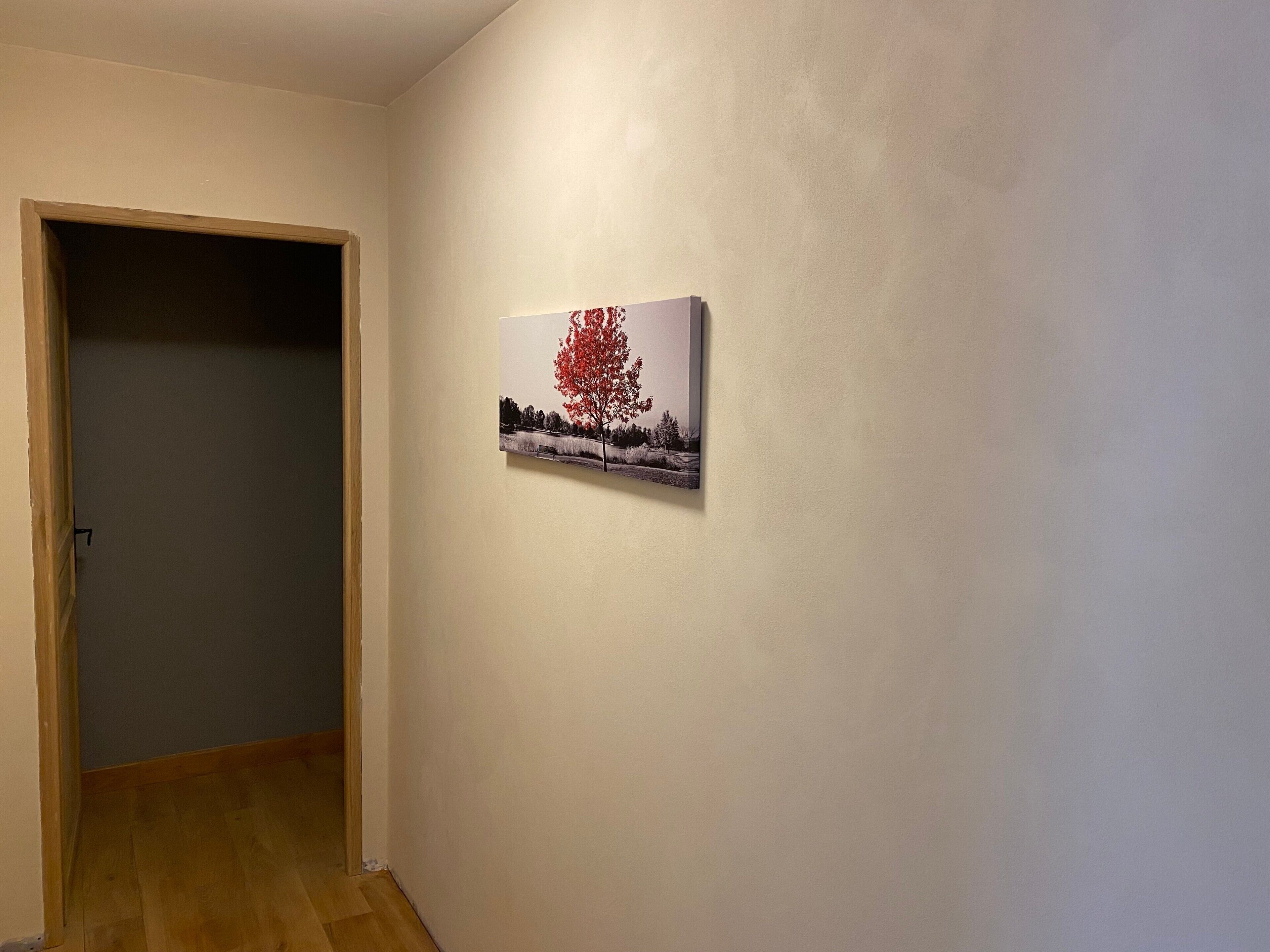 Un pasillo con una puerta de madera, un cuadro de un árbol colgado en la pared y un banco.