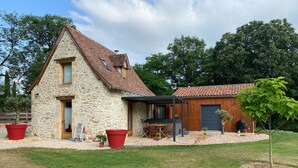 Een stenen huis met pannendak, een houten garage, en een terras met tuinmeubilair.