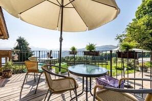 A deck with a round table, wicker chairs, a large umbrella, and a view of the mountains. - Apartment 'Monte Altissimo' with Mountain View, Shared Terrace and Wi-Fi (Brentonico)