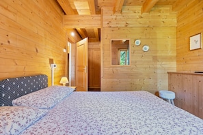 Une pièce de style cabane en bois, comprenant un lit, une table de chevet, un petit tabouret et une porte donnant accès à une salle de bain.