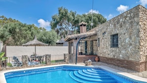 A stone building with a swimming pool, a covered outdoor seating area, and a view of trees.