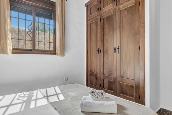 Une chambre avec une grande armoire en bois, une fenêtre avec des rideaux et un lit sur lequel sont pliées des serviettes.