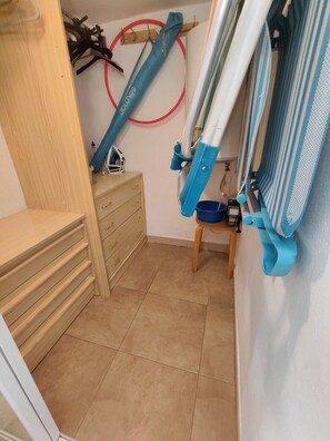 Une petite pièce avec une commode en bois, une planche à repasser bleue et un objet circulaire rouge accroché au mur.