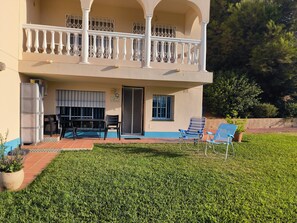 A two-story building with a balcony, a small patio with chairs, and a well-maintained lawn.