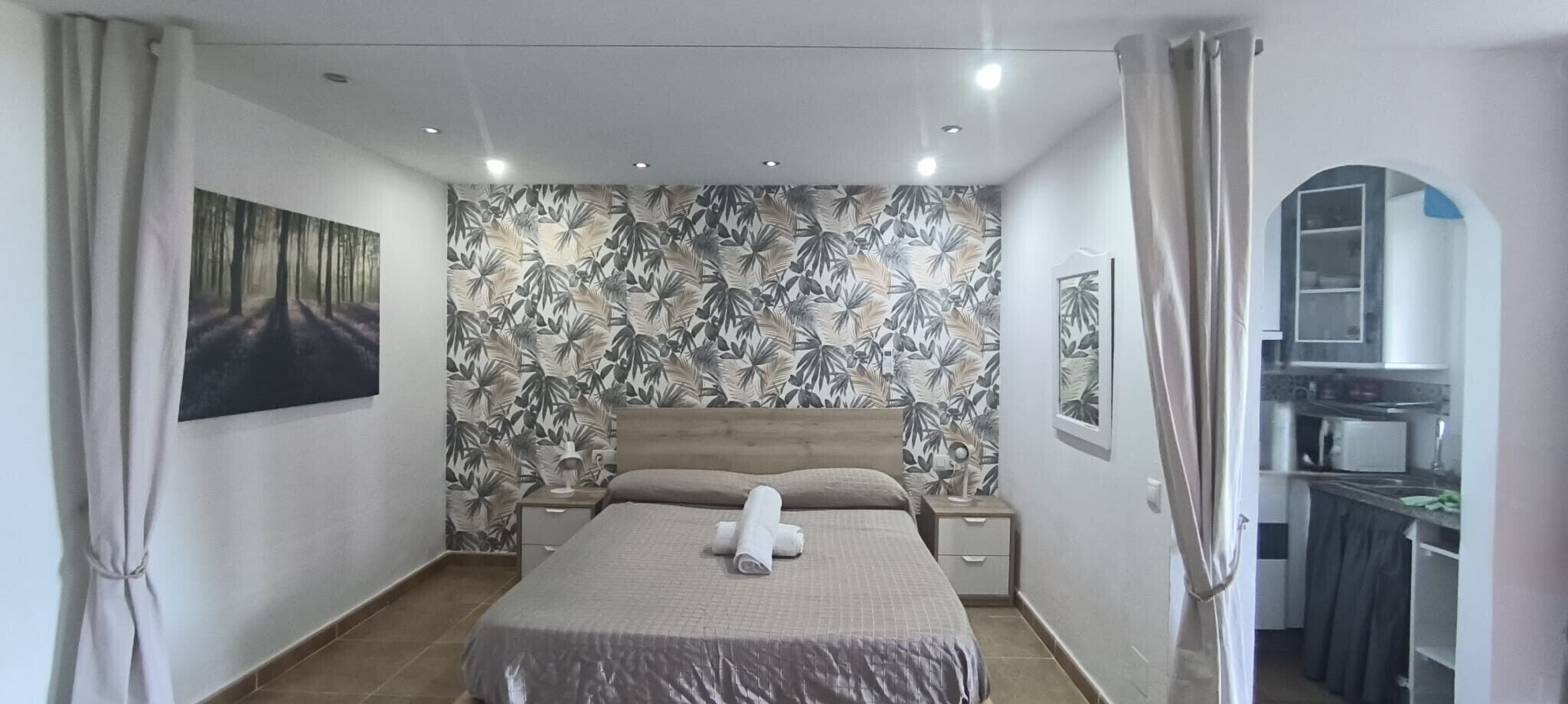 A bedroom with a bed, a nightstand, a wall-mounted lamp, and a painting.