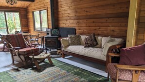 Interior acogedor de una cabaña con piso de madera, un sofá, un sillón mecedor, una mesita y una chimenea.
