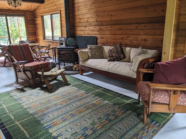 Ein gemütliches Blockhaus-Interieur mit Holzboden, einer Couch, einem Schaukelstuhl, einem kleinen Tisch und einem Kamin.