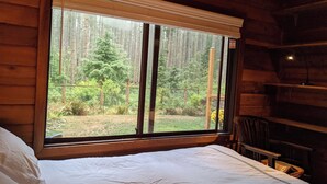Una habitación de cabaña de madera con un ventanal grande que da a una zona boscosa.