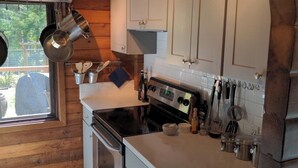 Cocina pequeña con armarios blancos, estufa y ollas colgantes.