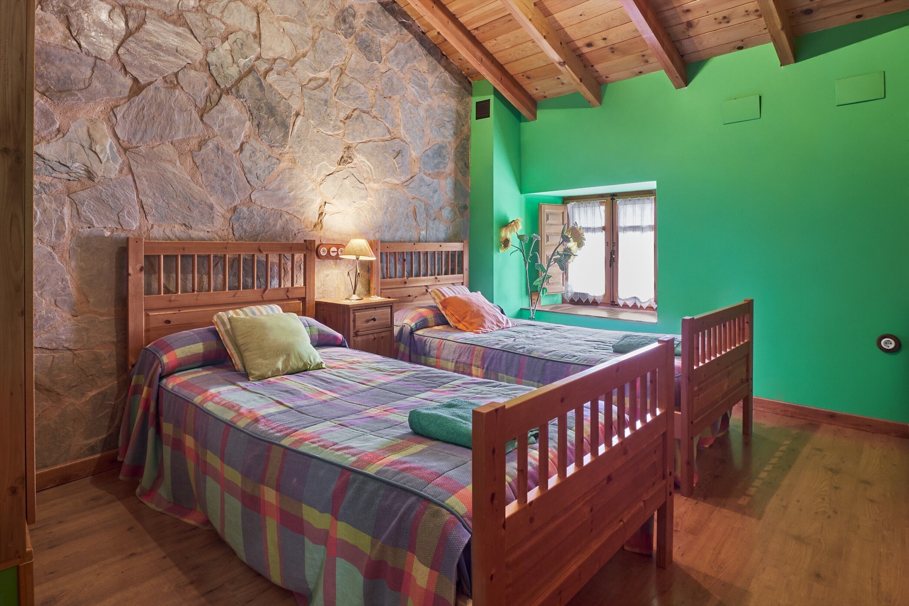 Una habitación con dos camas de madera, una pared de piedra, una pared verde y un techo de madera.