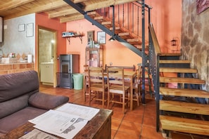 A cozy living area with a sofa, wooden dining table, chairs, a staircase, and a kitchen area. - Country Home 'Entre Valles' with Mountain View, Private Terrace and Wi-Fi (Benllera)