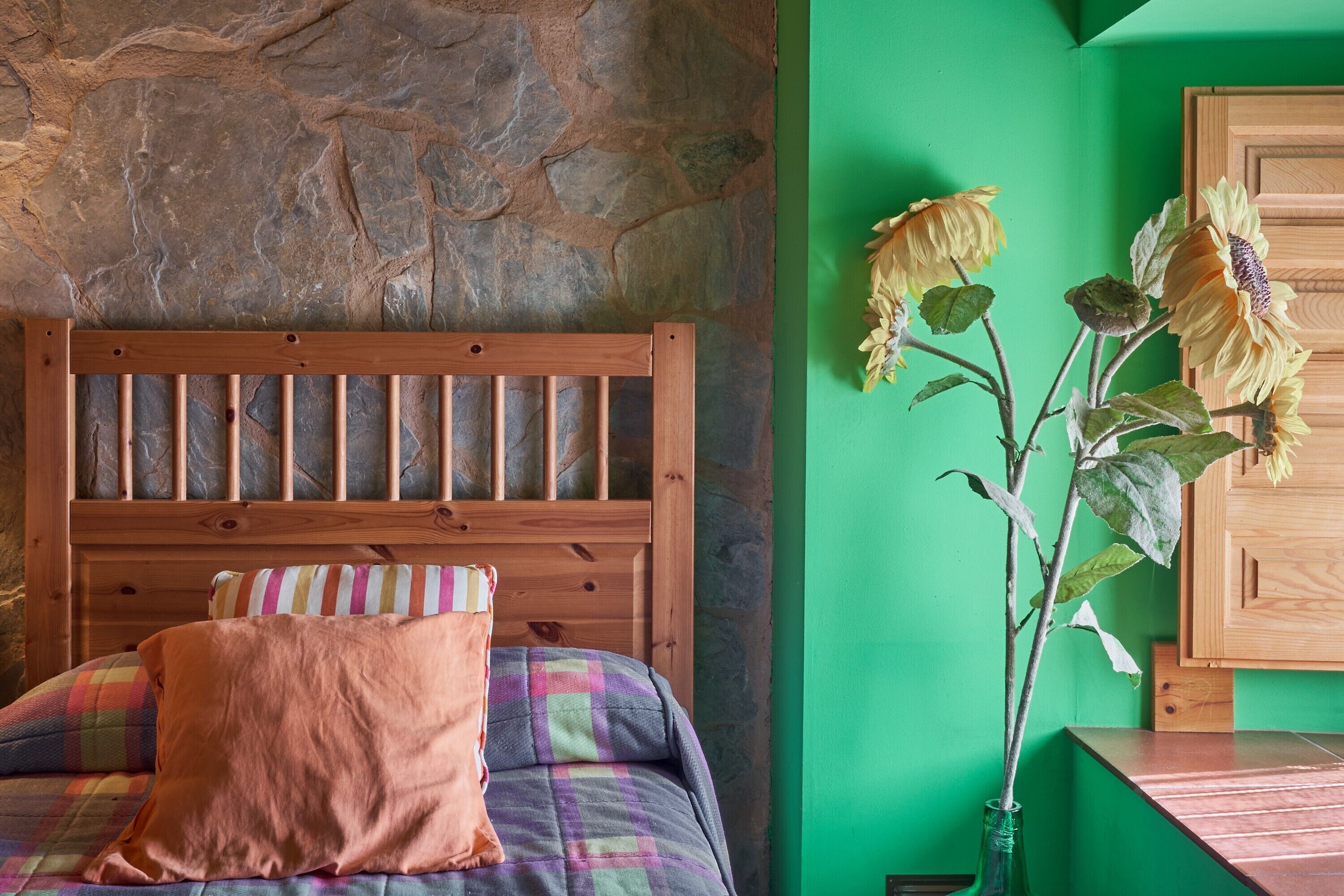 Une pièce avec un mur en pierre, un lit en bois avec un oreiller à rayures et un mur vert décoré de tournesols.