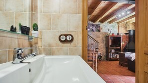 Une salle de bain avec un lavabo blanc, une étagère en verre où sont rangés les articles de toilette et un mur en pierre.