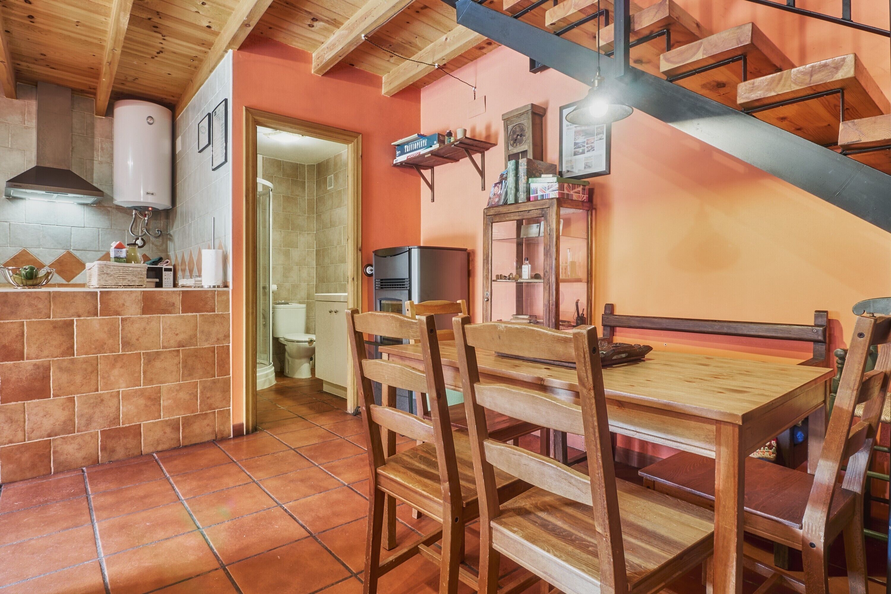 Uma cozinha com azulejos na parede, cadeiras e mesa de madeira, fogão embutido e uma escada.