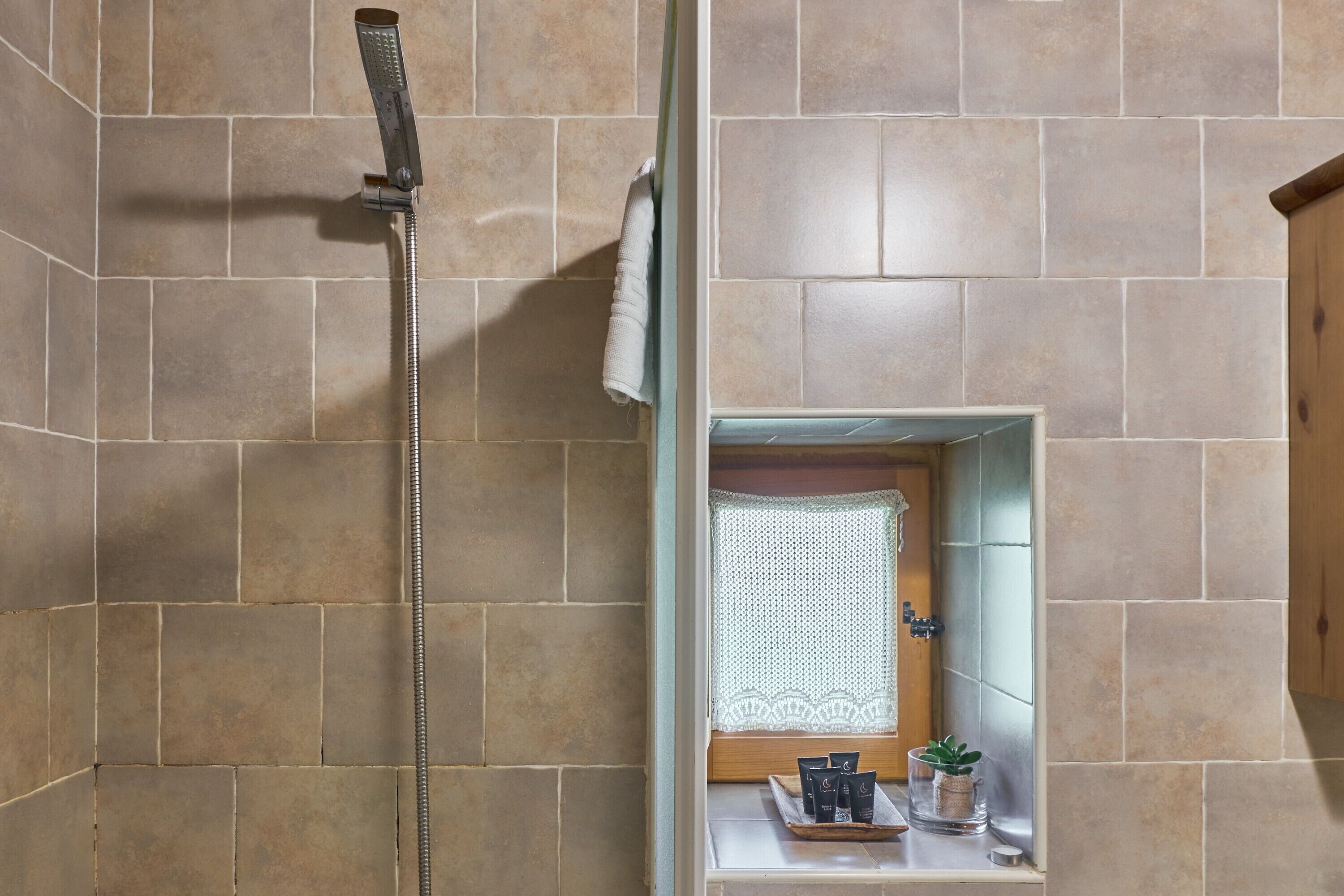 Une douche avec un pommeau de douche amovible, une serviette accrochée au mur et une petite étagère contenant des articles de toilette.