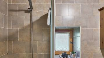 Une douche avec un pommeau de douche amovible, une serviette accrochée au mur et une petite étagère contenant des articles de toilette.