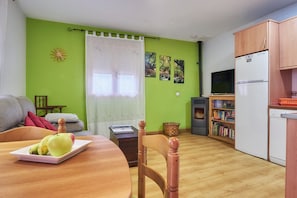 Un espace de vie compact comprenant un coin repas, un canapé, un téléviseur, un réfrigérateur et une bibliothèque.