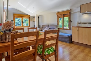 A dining area with wooden chairs and a table, a sofa, and a kitchen area with wooden cabinets.