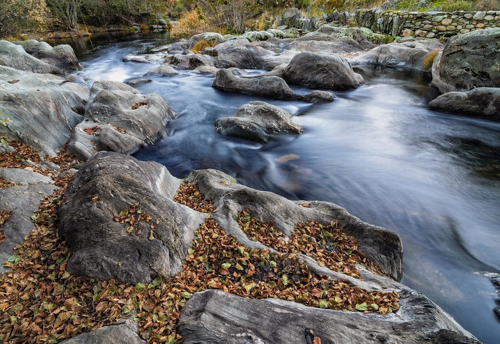 A river flowing through a rocky landscape with autumn leaves scattered around.
